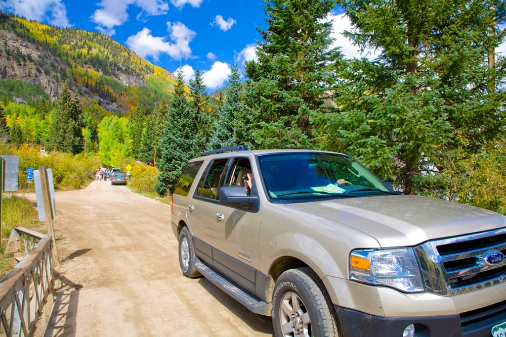 A car drives across a small bridge with mountains and blue sky in the background