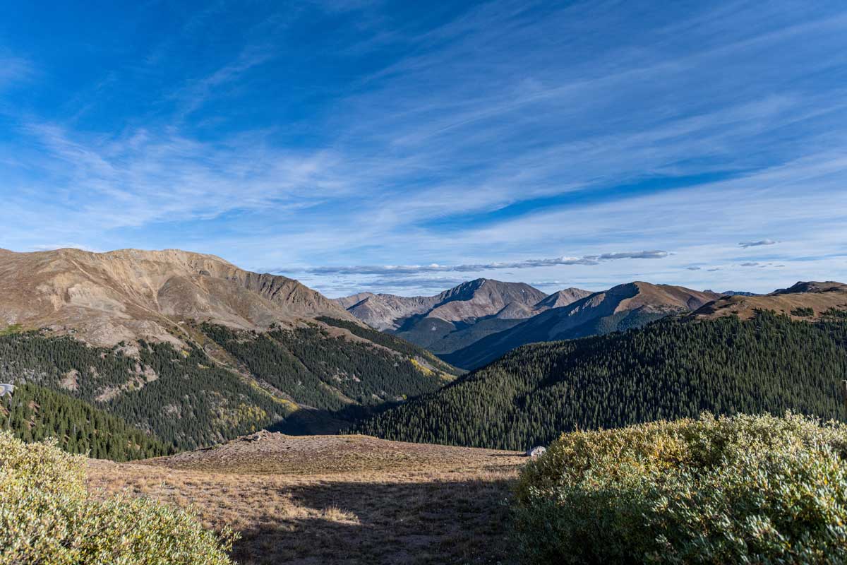A scenic outlook offers views of forest-covered mountains along the Independence Pass near Aspen and Leadville, Colorado. The sky above is blue and streaked with clouds.