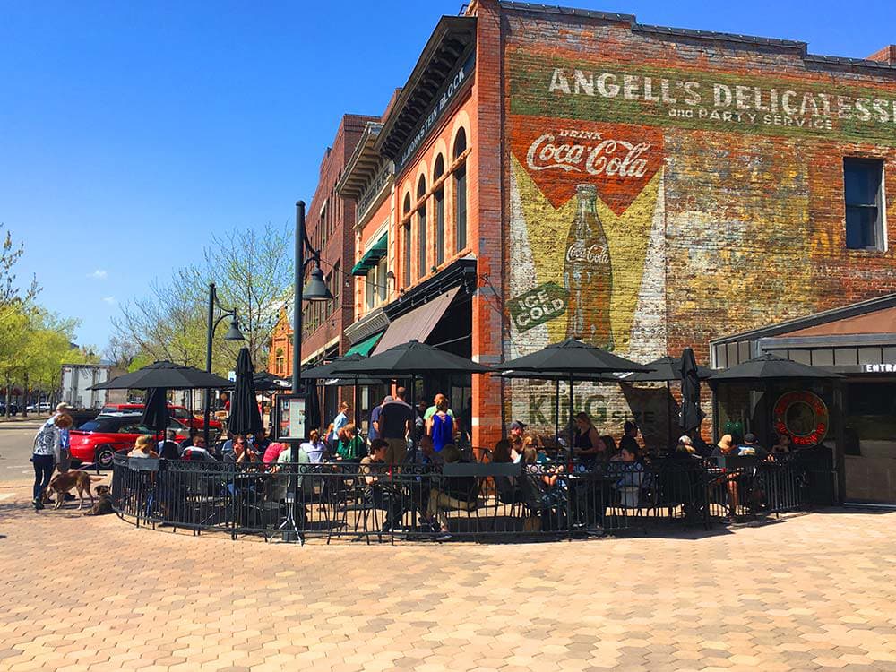 A black-umbrella-covered patio shades diners outside the large, old-looking brick building of CooperSmith's Pub & Brewing restaurant in Fort Collins, Colorado.