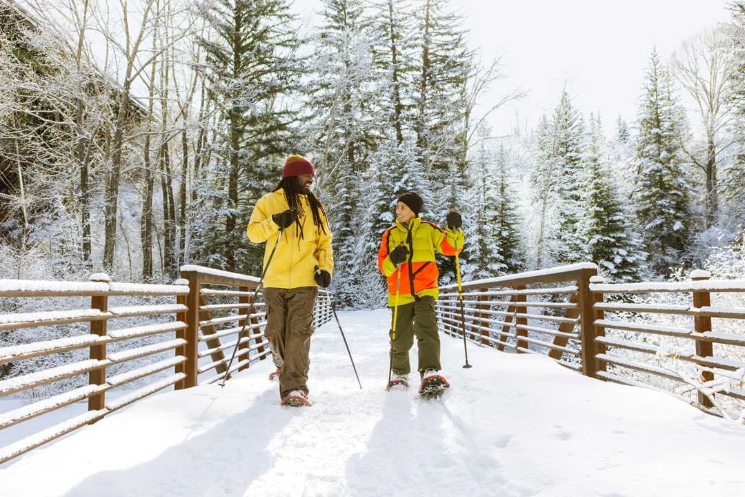 Two people snowshoe across a snow-covered bridge