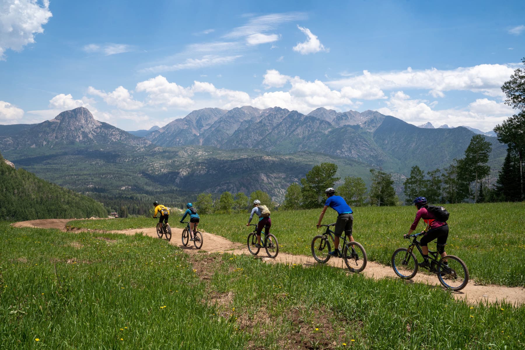 group of mountain bikers riding down trail with stunning mountain views photo 14
