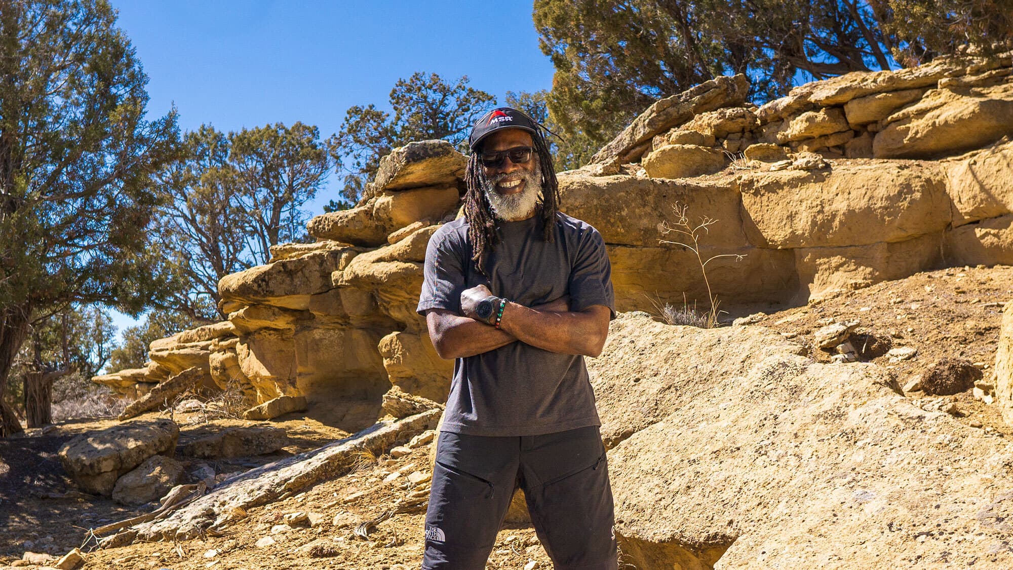 Man standing on a trail on a desert setting surrounded by evergreens