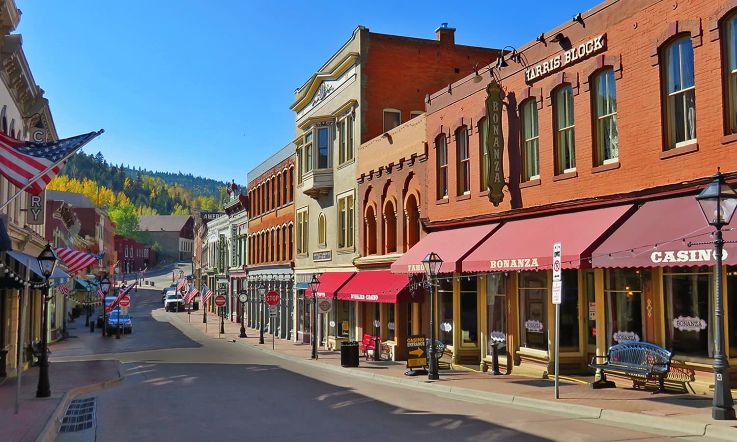 Main Street of downtown Central City on a summer day. Red-brick Victorian-era buildings with red awnings line the street.