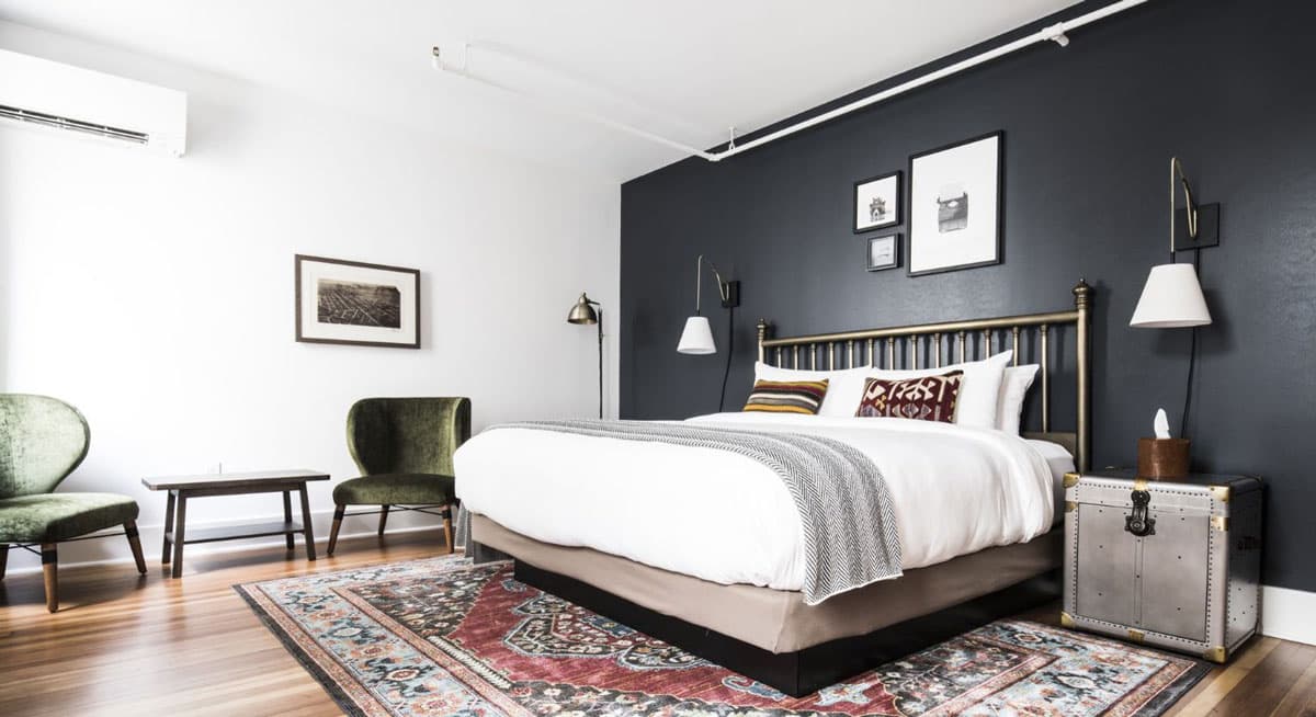 The deluxe king suite at The Armstrong Hotel in Fort Collins, Colorado with a cozy king bed flanked by chic nightstands and decorated with framed artwork and a cheery patterned rug.
