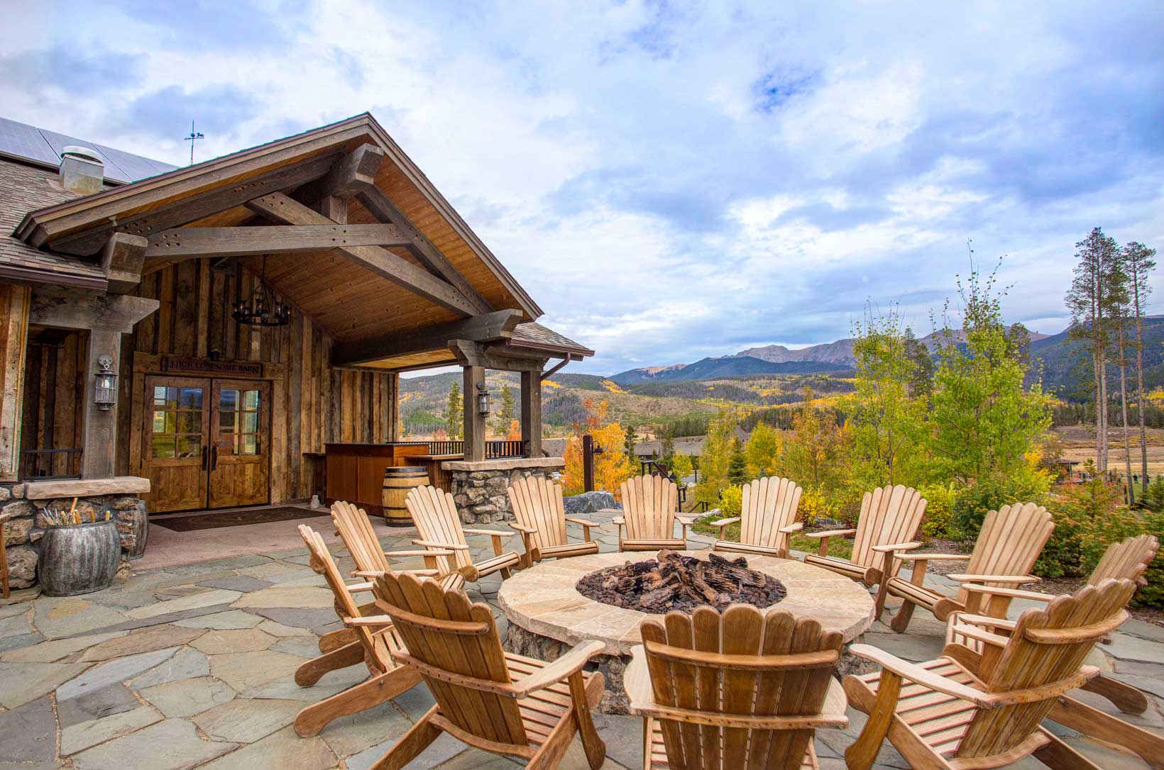 Adirondak chairs surround a fire bit in front of a wooden lodge's entrance