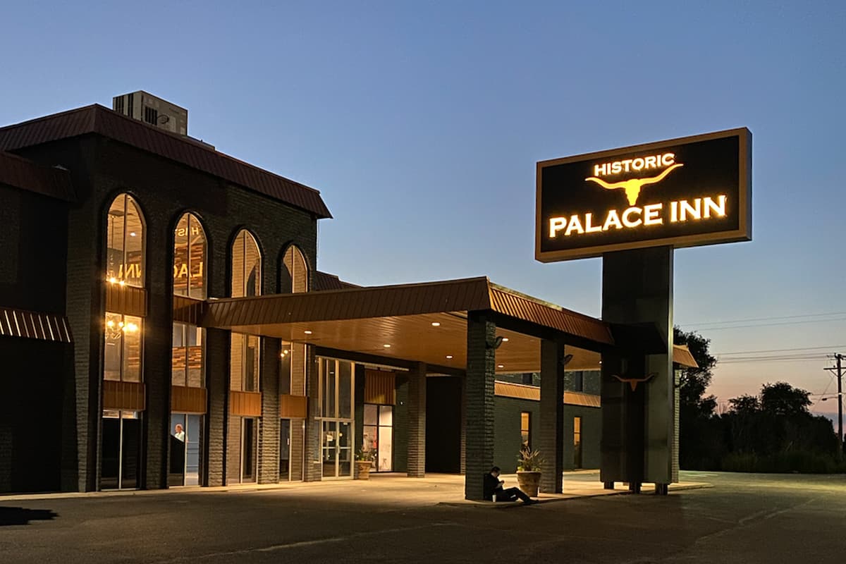 As the last rays of the sun fade in the distance, the sky darkens around a tall, light up hotel in Lamar, Colorado with a big sign that says, "Historic Cow Palace Inn."