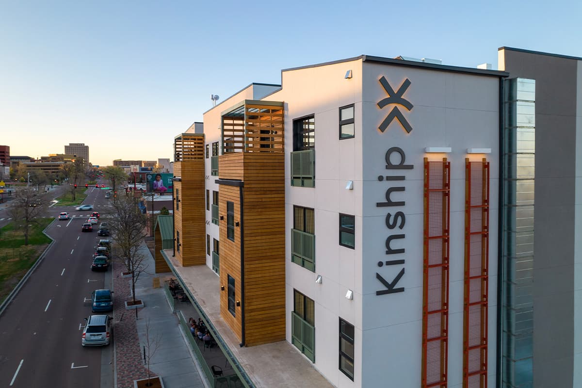 Kinship Landing is a multi-story hotel set on the edge of Colorado Springs. The white building is modern with wood-panel accents.