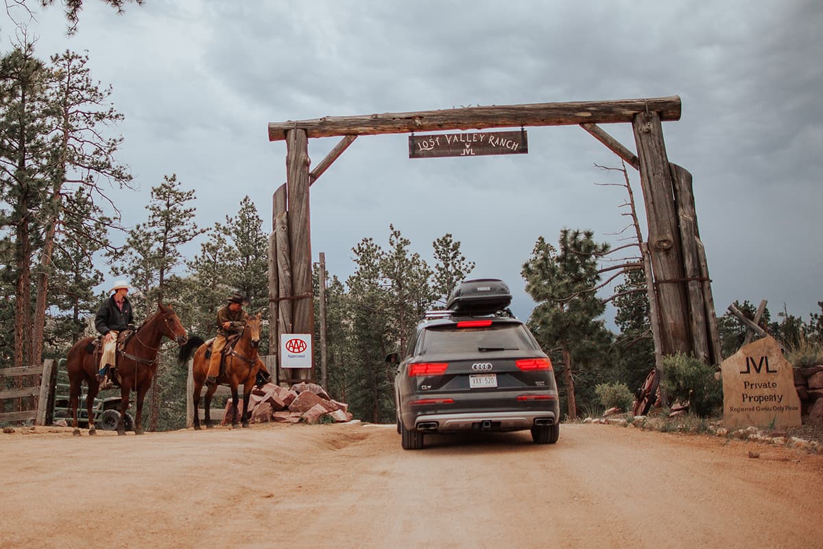 Two ranch hands sit on horses and welcome guests as they drive through the entrance to Lost Valley Ranch.