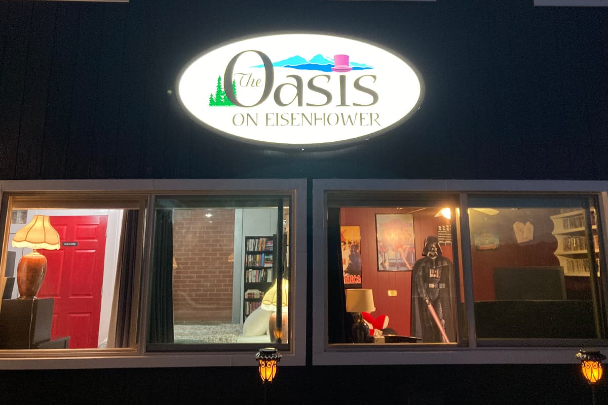 A backlit sign for The Oasis on Eisenhower glows brightly above two curtainless windows in Loveland, Colorado.
