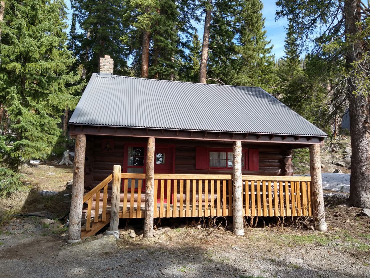 A rustic Grand Mesa Lodge cabin with a welcoming front porch is surrounded by evergreen trees.