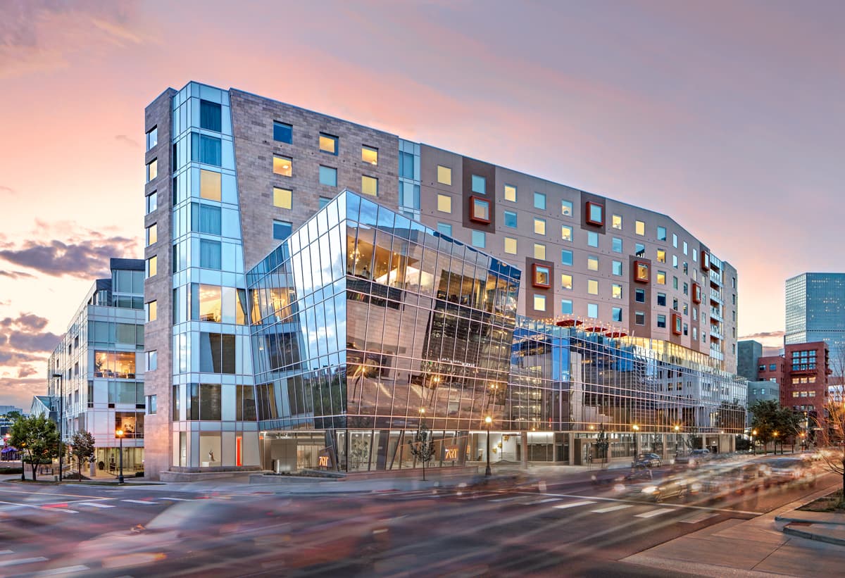 The Art's many-windowed walls reflect sunset over Denver. The sky is fiery in shades of pink and yellow.