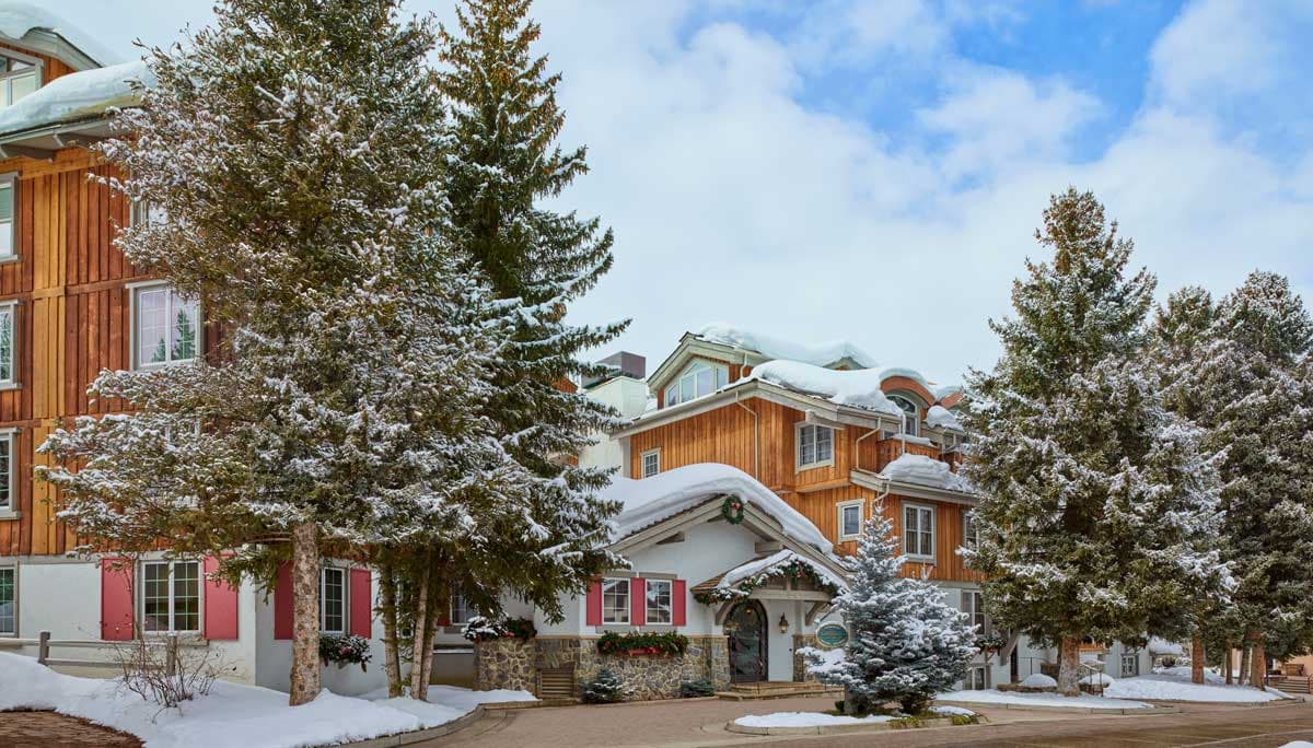 A snowy exterior view of Christiania at Vail with lofty pine trees in the foreground