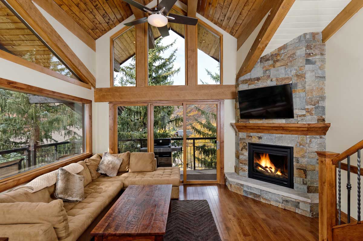 A living stylish living room with floor-to-ceiling windows and a stone fireplace at The Crestwood Condominiums in Snowmass Village.in