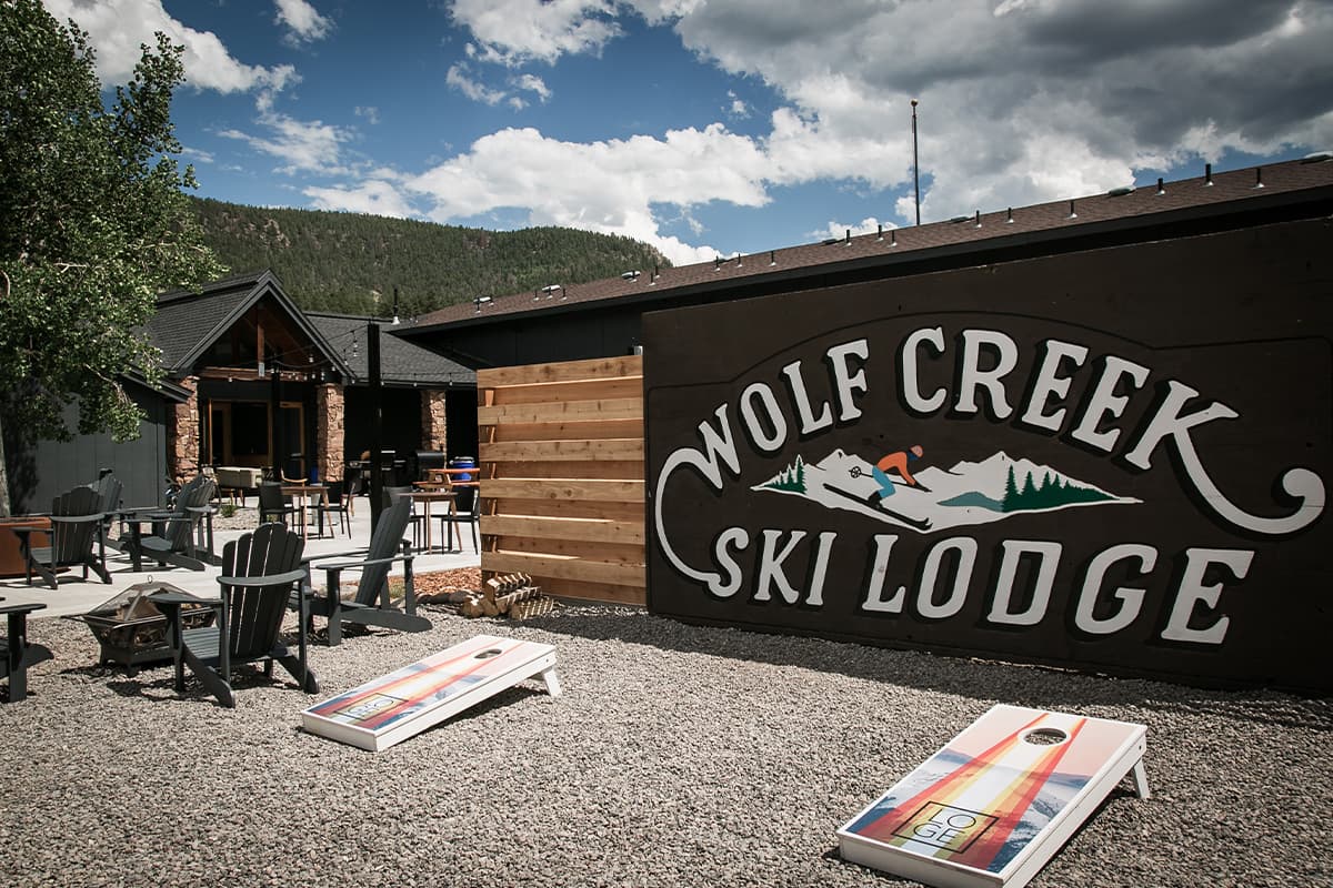 Beneath a cloud-studded blue sky near South Fork, Colorado, a large sign with a skier on it reads, "Wolf Creek Ski Lodge"