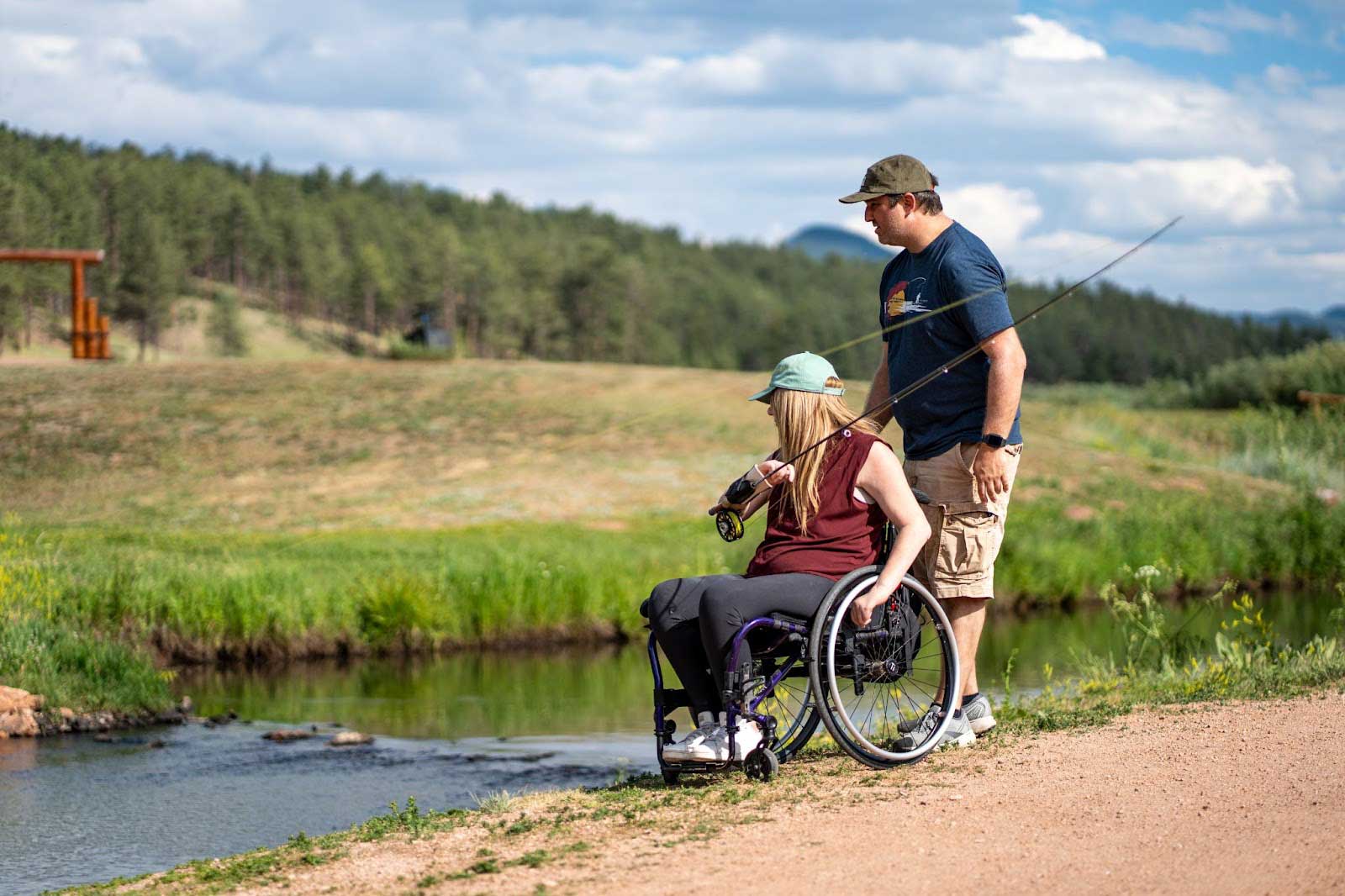 A person in a wheelchair is pushed alongside a riverbank