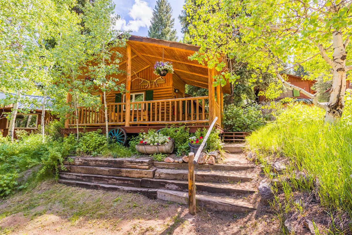 A rustic log cabin at Tumbling River Ranch near Grant, Colorado, peeks out between branches of young aspens.