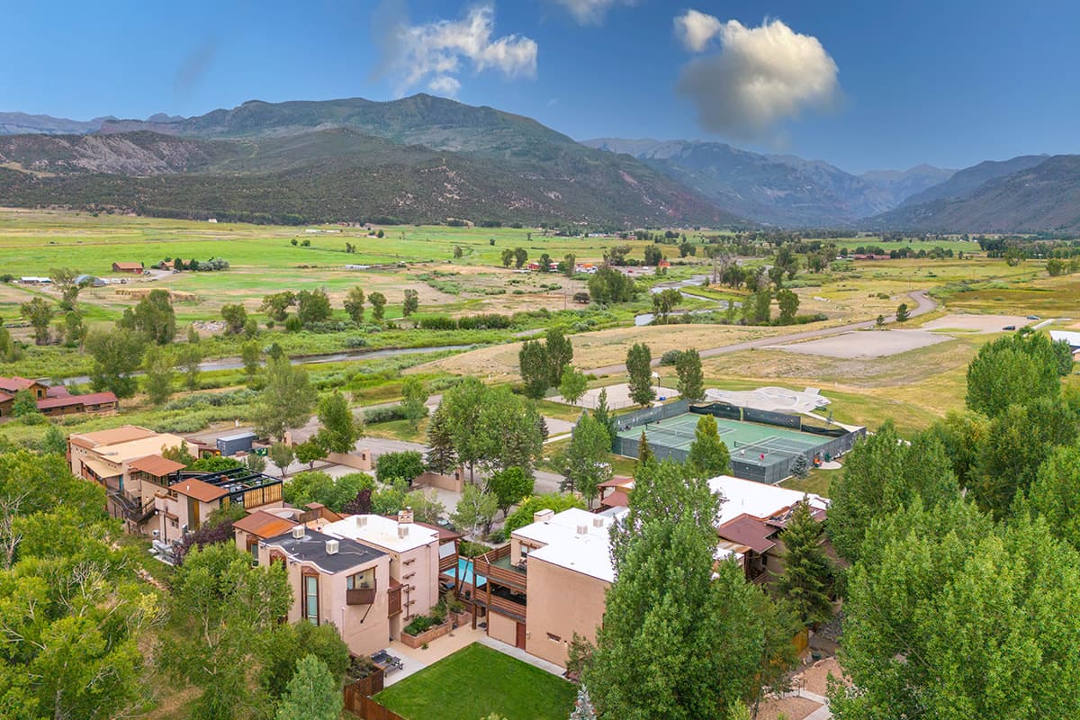 An aerial view of the Chipeta Lodge Resort + Spa in Ridgway, Colorado, showcases a stunning, natural setting with aspens, pines, fields and distant peaks.