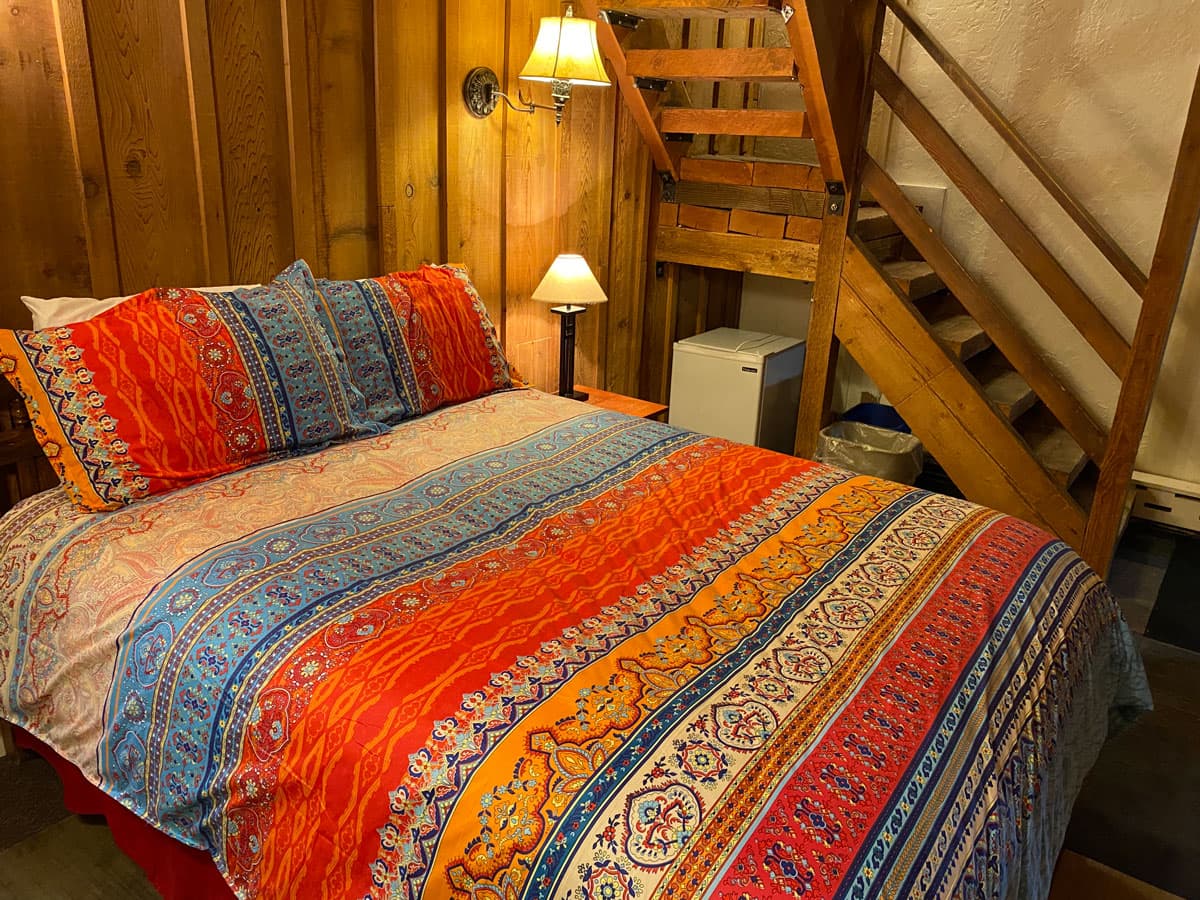 A cozy bed is covered in a green, orange, yellow and white blanket at The Nordic Lodge.