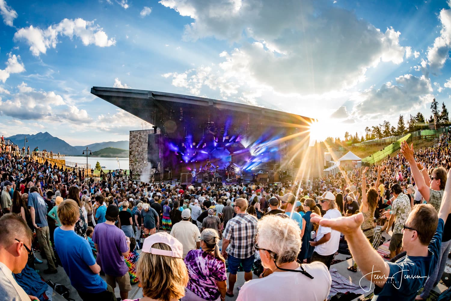 A crowded summer concert at Dillon Amphitheater. The sky is blue with clouds and the sun is bright on the right side of the stage.