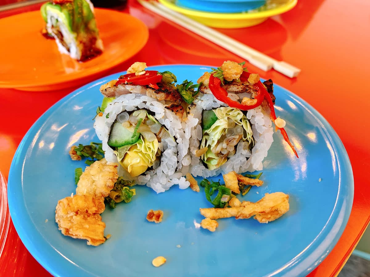 Colorful sushi rolls, filled with vegetables and breaded fish, sit on a blue plate with chopsticks in the background at Sushi-Rama in Denver's RiNo neighborhood.