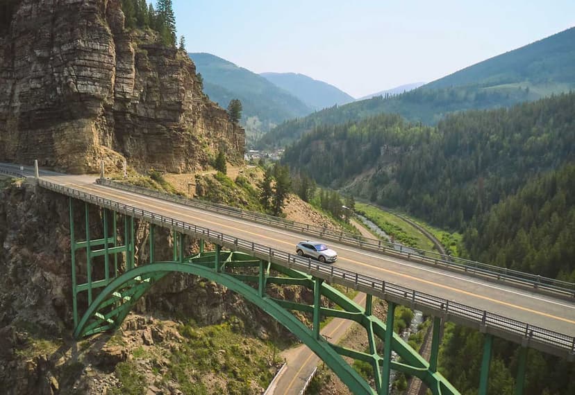 A car drives across a bridge in Colorado with rolling mountains in the background on the way to Red Cliff