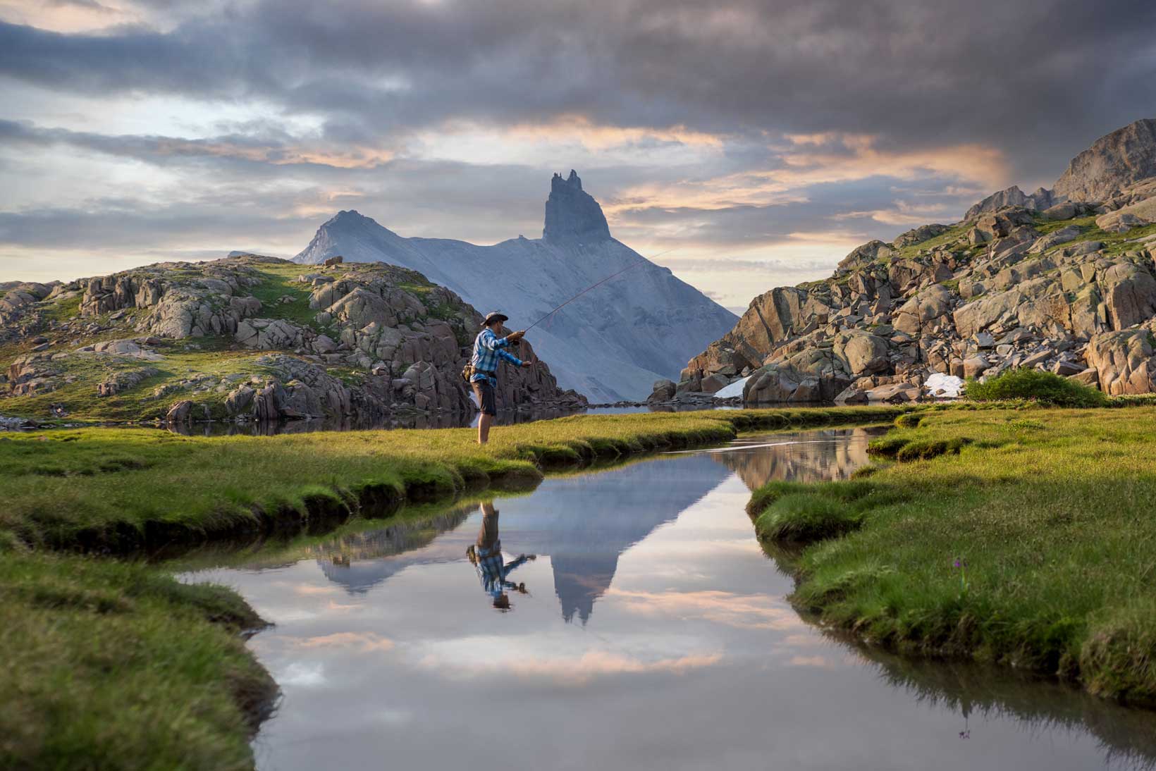 A man fishes on the banks of a smooth-as-glass river