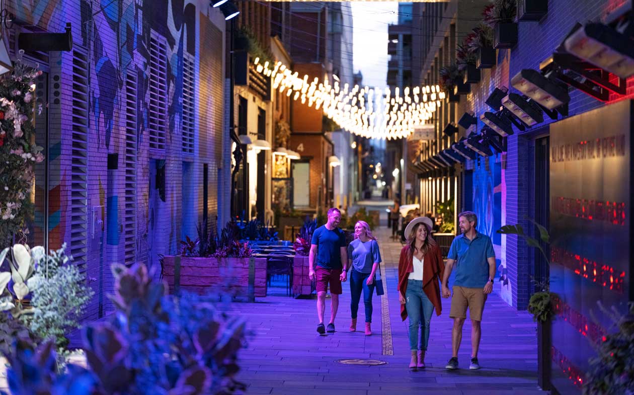 Couples walk through an alleyway lit with white lights