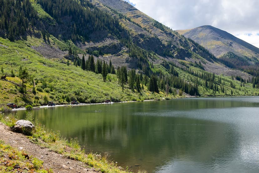 A still lake beneath two hills covered in evergreen trees in Pitkin, CO