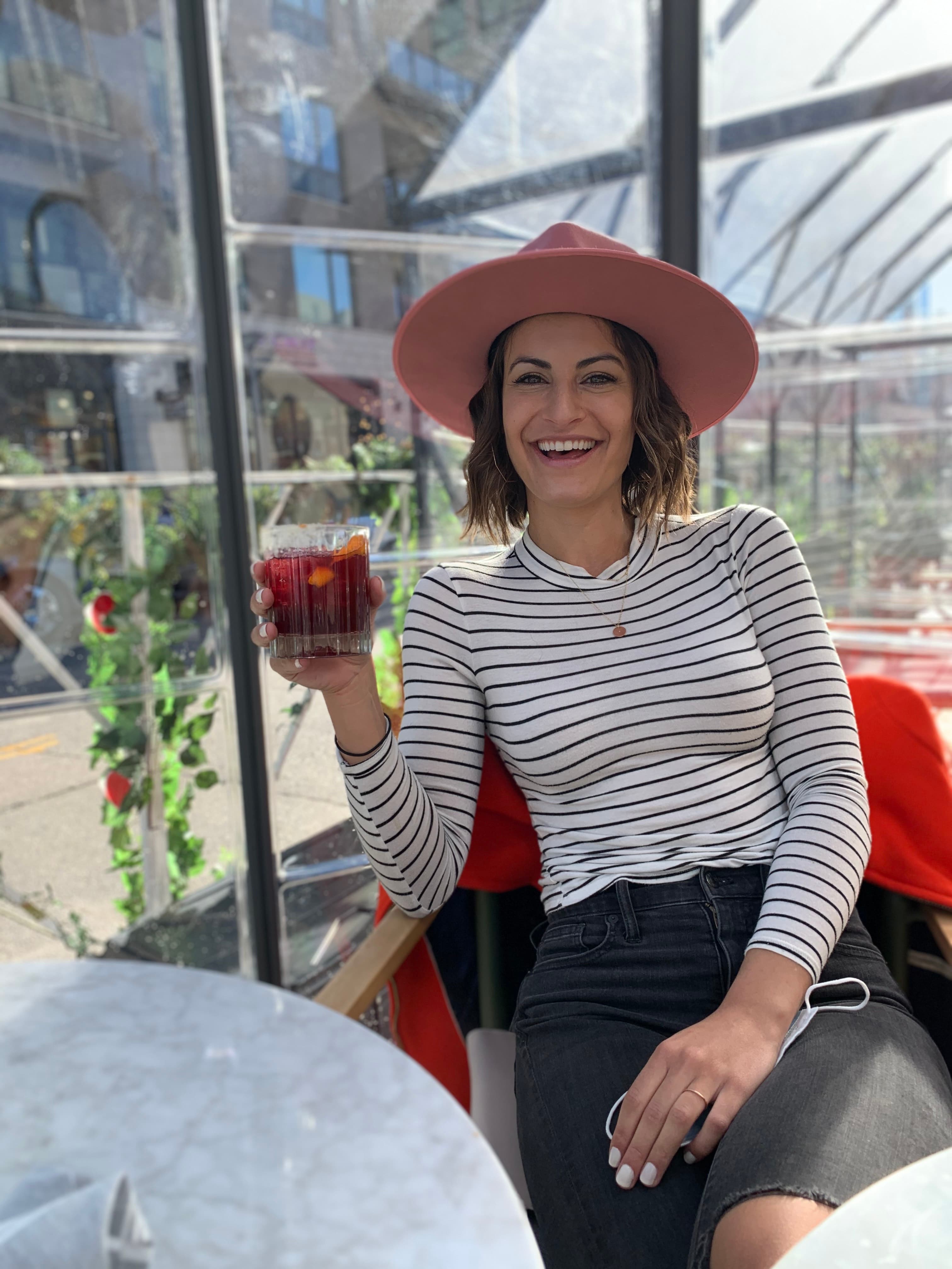 A person in a long sleeve striped shirt and hat laughs on a chair under the sun with a drink in hand at the Halcyon.