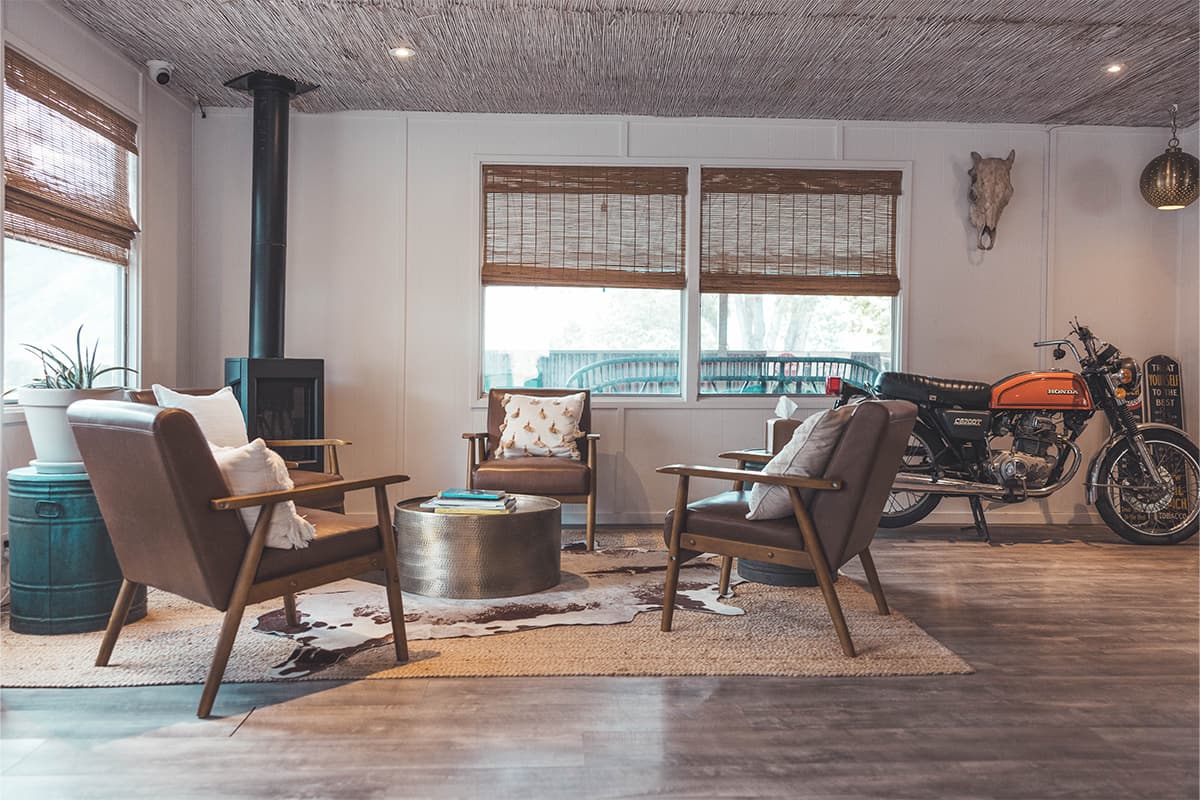 A cozy common area at Basecamp 550 features a metal stove, four leather chairs with pillows and a decorative motorcycle.