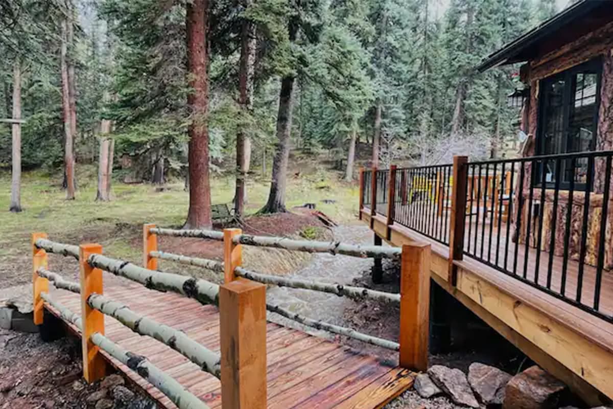 A bridge with aspen-branch railings goes over a cascading creek and leads to a cabin near Conifer, Colorado.