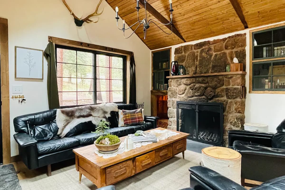 A stone hearth is surrounded by plush, black-leather couches and rustic decor at a cabin near Conifer, Colorado.