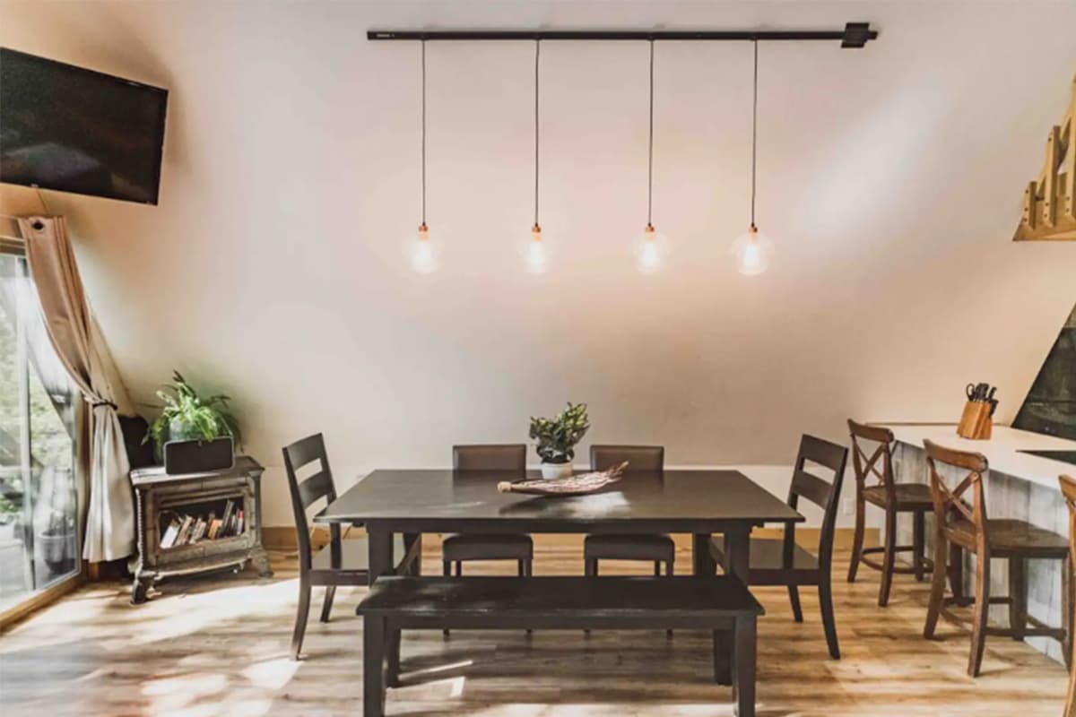 Four exposed bulbs hang over a dark wooden table with matching chairs and a bench. The dining area could comfortably seat six people.