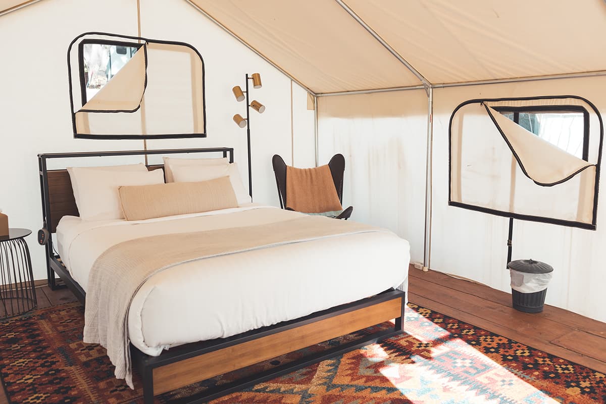 A glamping tent is set up with zippable window flaps, a plush white bed and a comfy chair at Basecamp 550 in Colorado.