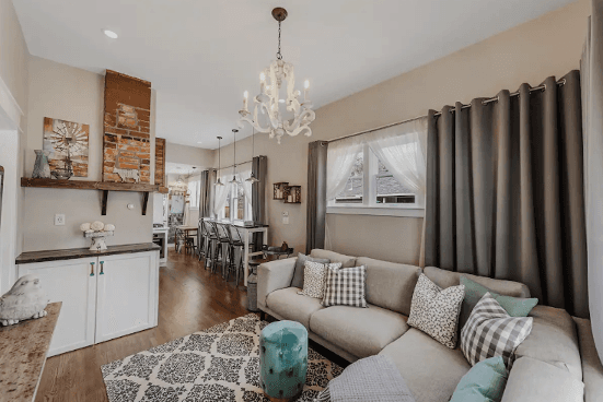 The Aggie House in Lousiville features an expansive couch in its living room along with a stylish chandelier