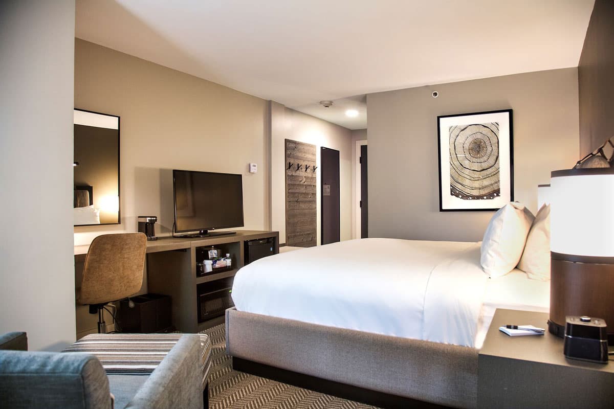 An interior photo of a hotel room with a king bed. The decorations are wooden and rustic and the bed is dressed in white linens.