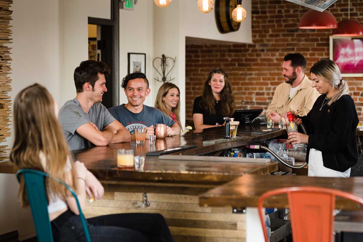A group of travelers gather around the bar to chat at Hostel Fish in Denver