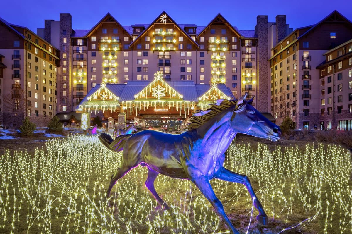 Gaylord Rockies Resort & Convention Center seen from the exterior with holiday lighting. A galloping horse statue is in the foreground.