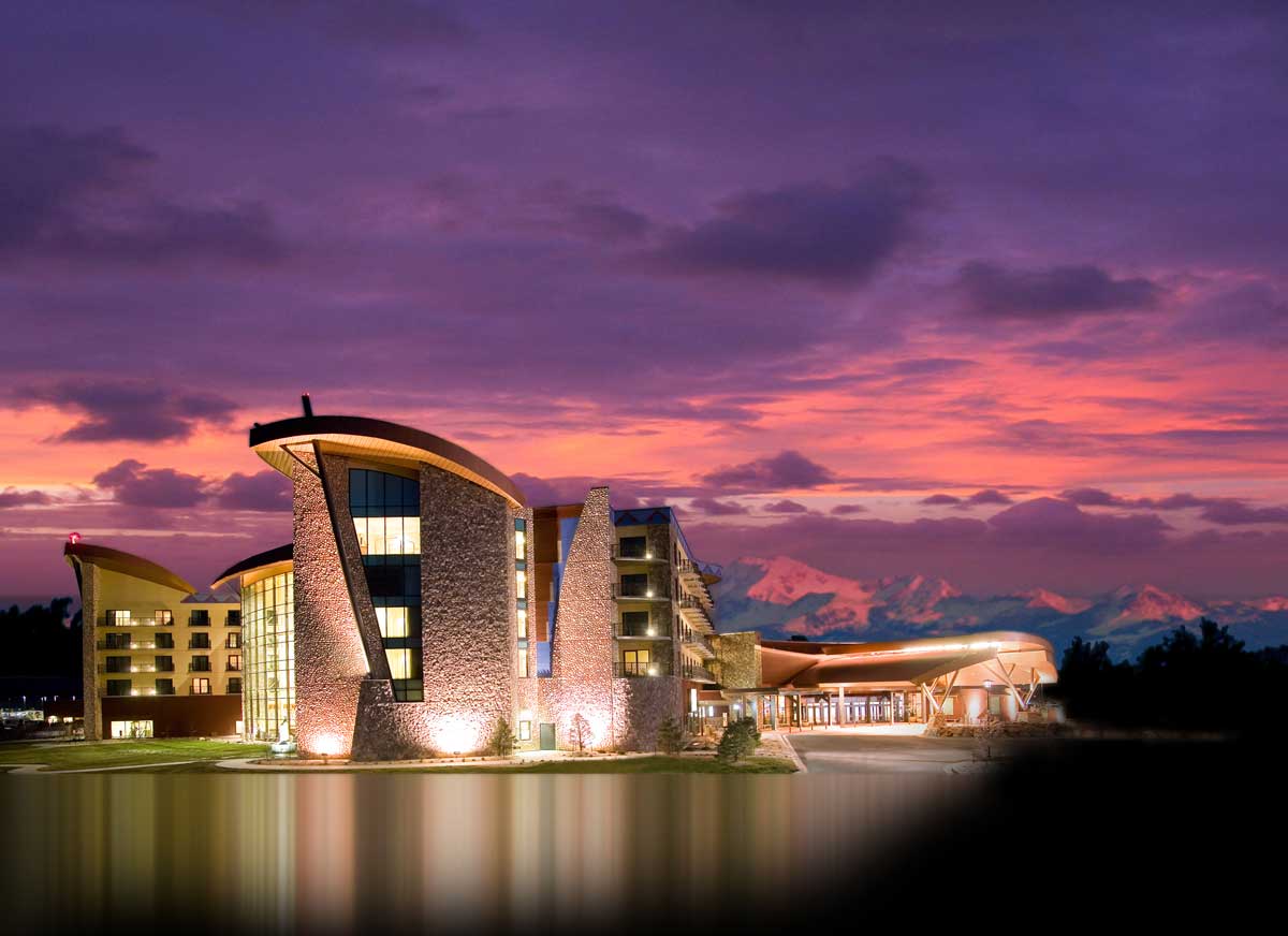 Sky Ute Casino seen from a distance with the sun setting behind; the sky is shades of violet and pink with mountains in the distance. 