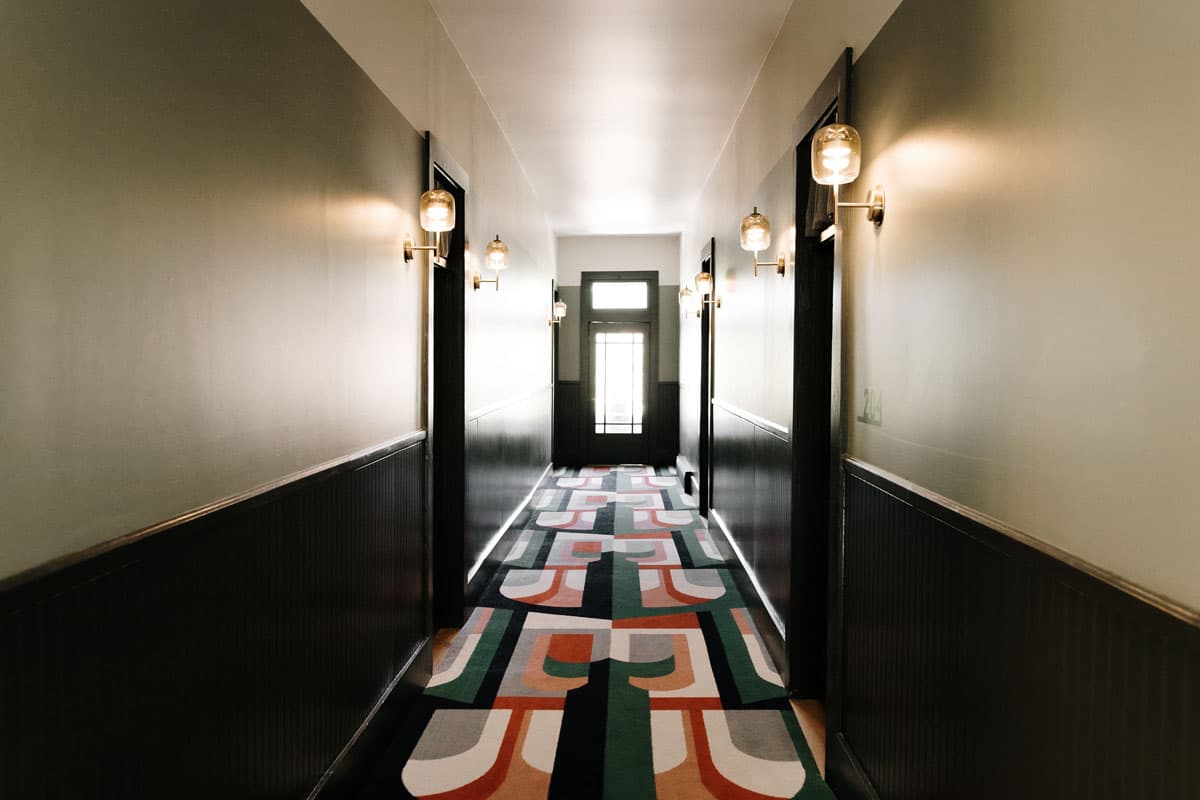 A long hallway with modern, geometric carpet and lighting on both sides atThe Rochester Hotel in Durango