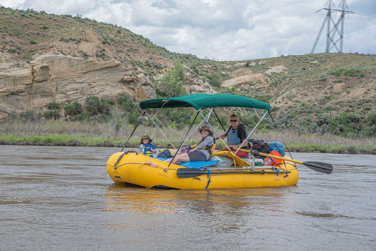 A family boating on Yampa River at Yampa River State Park with hills in the background