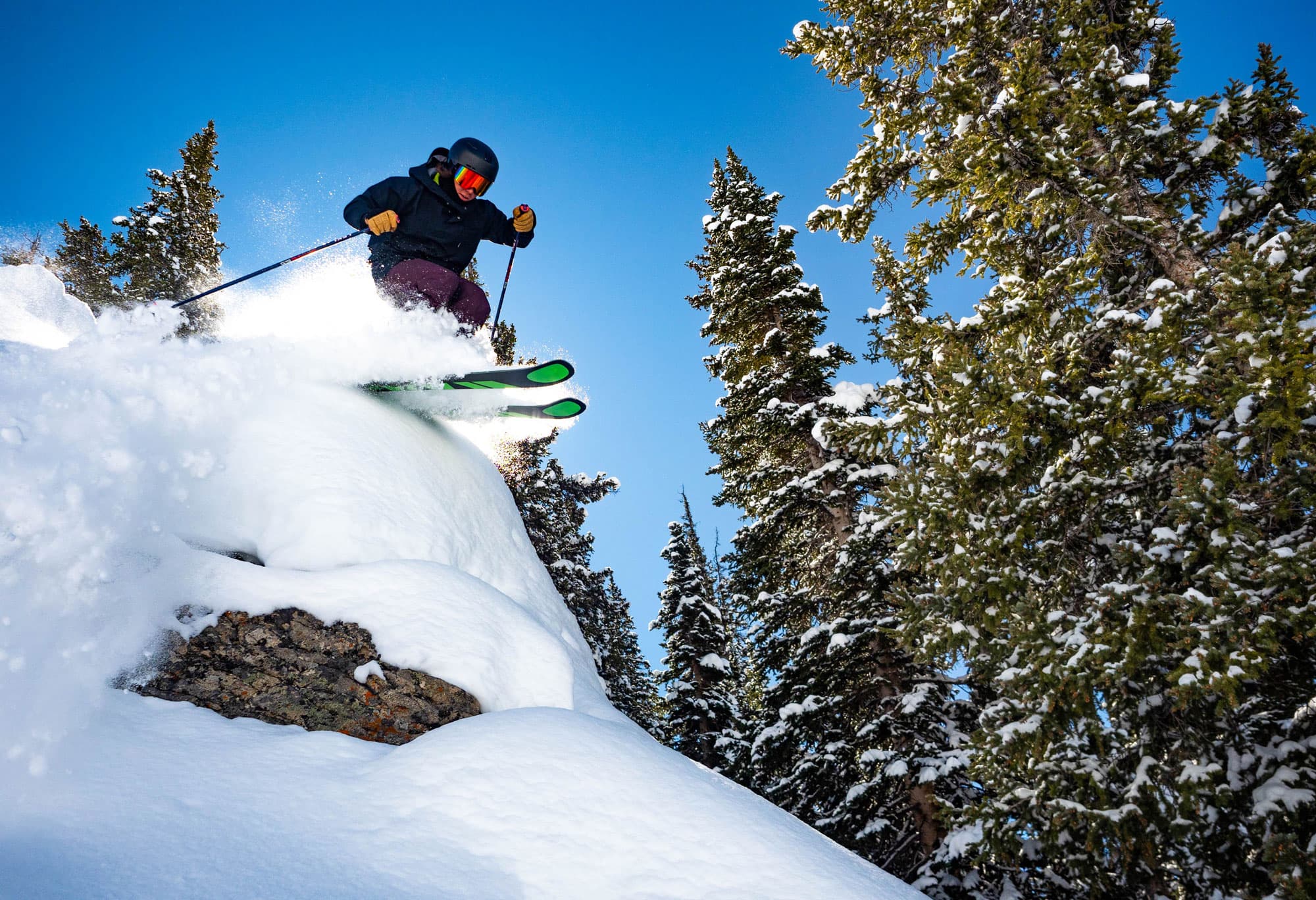 A skier about to make a jump going downhill with tall pines in the background in Gunnison and Crested Butte, Colorado.