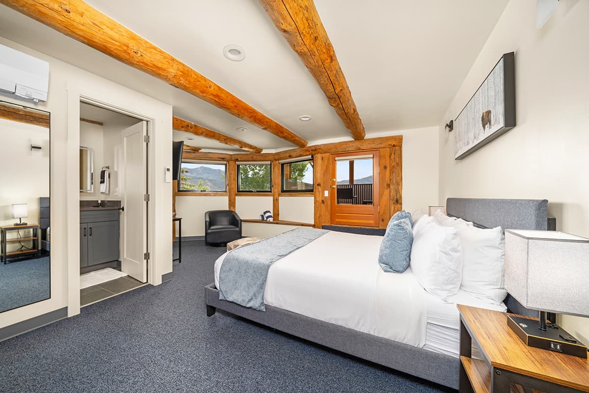 An updated guest room at the Chipeta Lodge Resort +Spa in Ridgway, Colorado, features stunning views, a balcony and exposed wooden beams.
