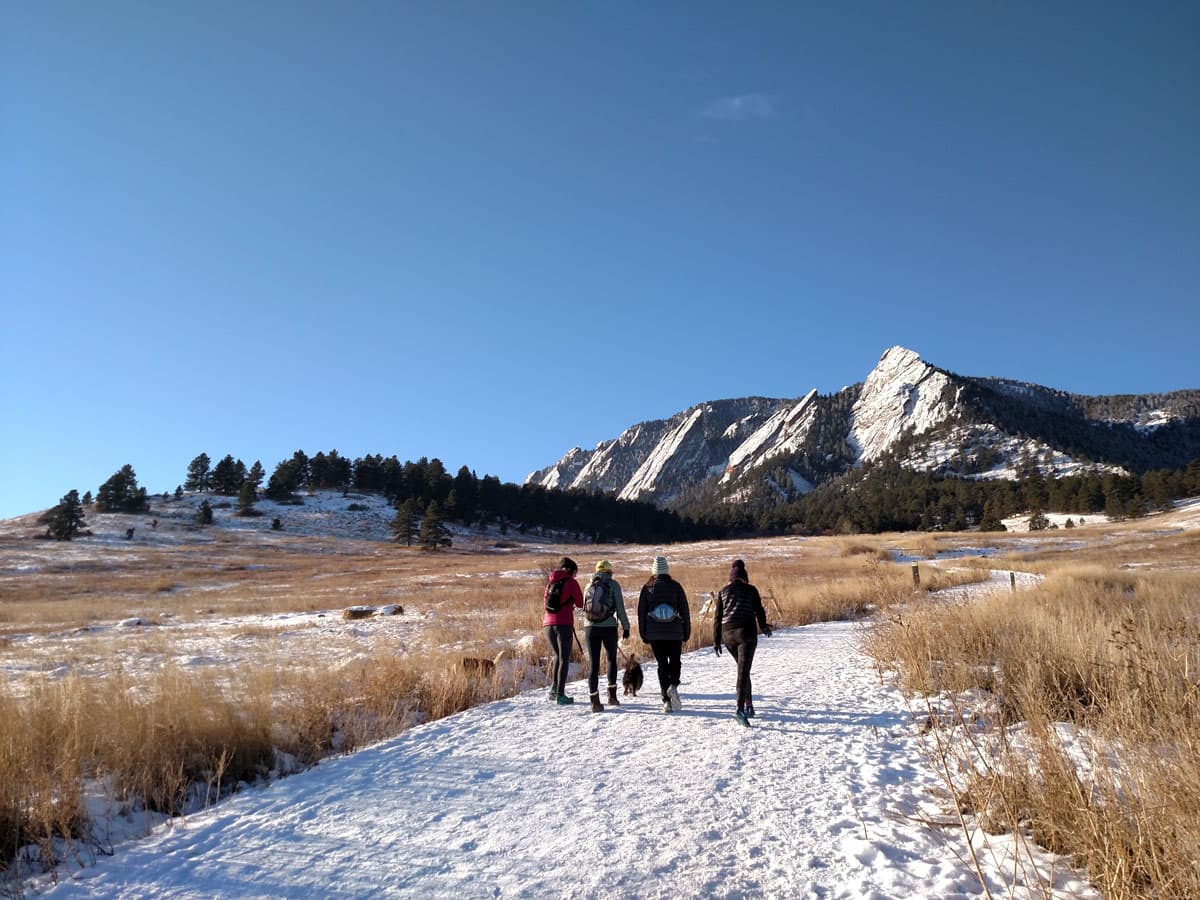 People walking with a dog towards the Flatirons during winter in Boulder, Colorado.