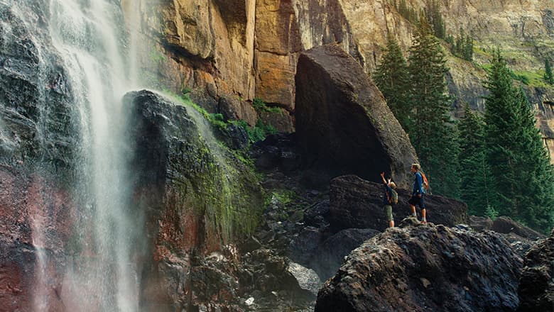 Two children raise their hands excitedly in front of rushing water of Bridal Veil Falls