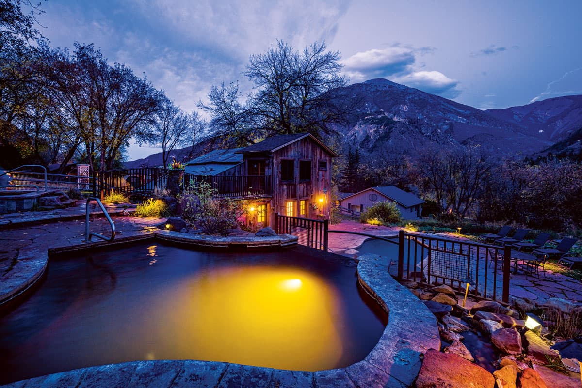 A hot spring pool with a stone-lined edge glows within from a yellow underwater light at Avalanche Ranch Cabins & Hot Springs in Colorado.