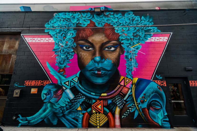 A mural on the side of a black-painted brick building in Denver, Colorado, features an person with vibrant turquoise flowers dripping down from their head.