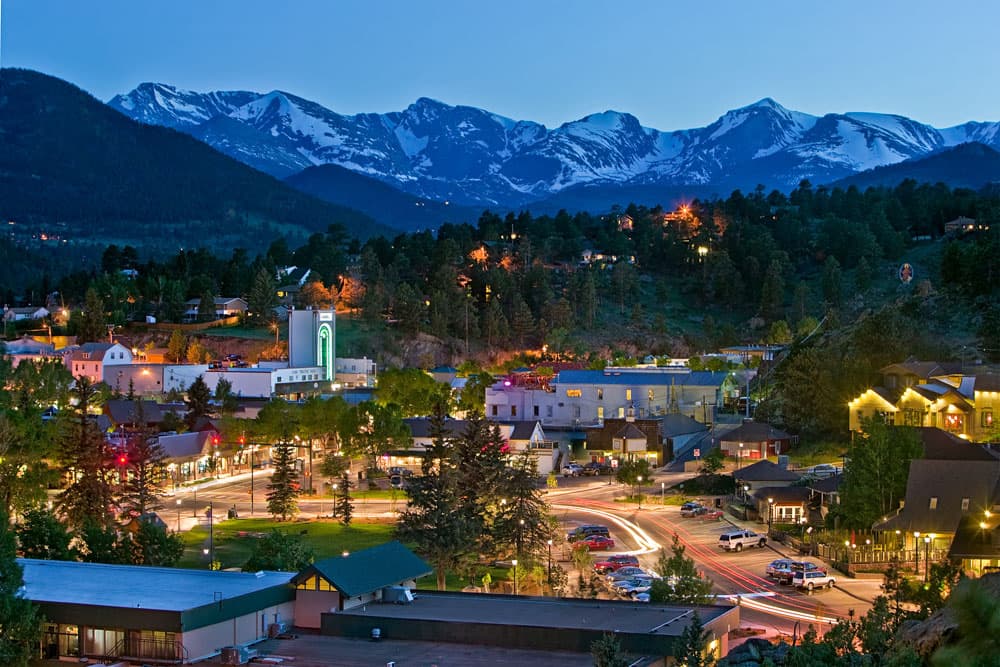 The snowy, white mountain appear to be aglow above the bustling, lit up town of Estes Park, Colorado. 