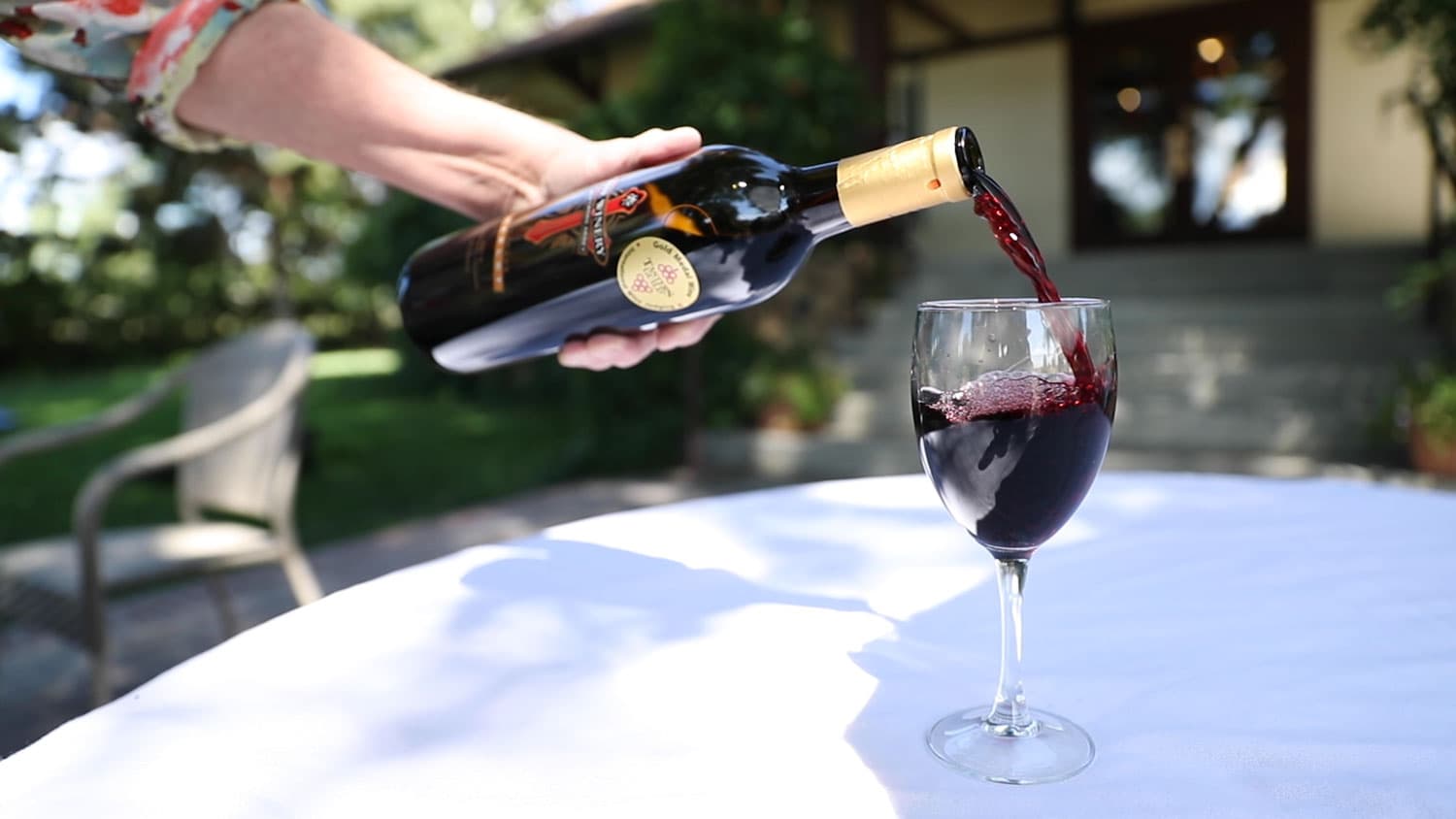 A person pours a bottle of red wine into a stemmed glass on the outdoor patio at the Winery at Holy Cross Abbey in Cañon City, Colorado.