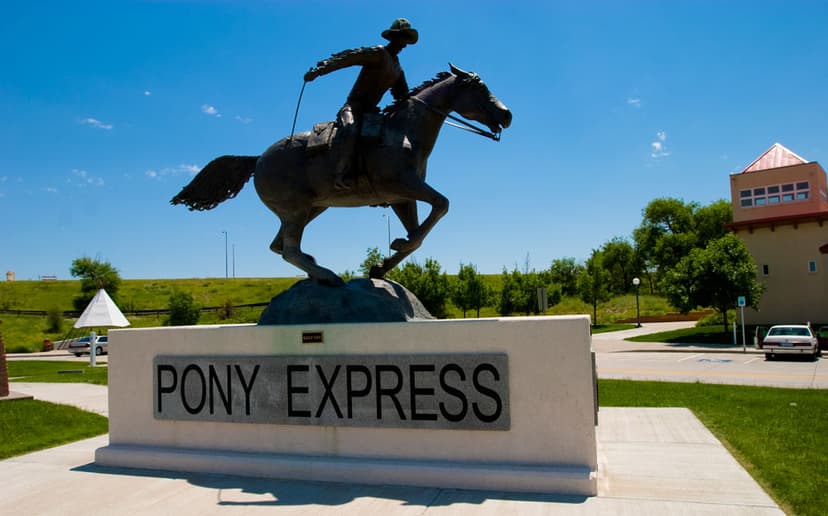 The Pony Express monument, which is a horse topped with a rider galloping full out atop a pediment that says "Pony Express." There's a blue sky in the background with green grass and trees. 